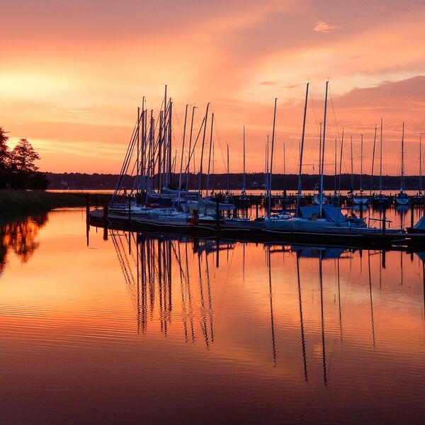 Ein kleiner Yachthafen mit Schiffen im Sonnenuntergang. Reflexionen auf dem Wasser.