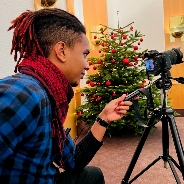 Das Bild zeigt den Mitarbeiter Moritz Rohwedder an der Kamera. Im Hintergrund steht ein festlich geschmückter Weihnachtsbaum.